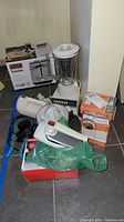 Lot of small kitchen appliances including boxed toaster, blender, hand mixers, can opener, juicer, and coffee grinder