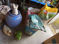 Overview of all items including vase, bags of fertilizer, tub of rock salt, and garden figures on concrete floor.