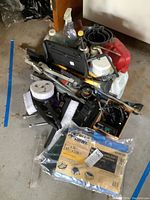 Photo shows collection of vehicle care tools including brushes, funnels, a floor jack, a radio, and other items piled together.