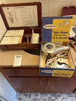 Photo showing Bethlehem Steel first aid kit wooden box with unopened bandages, metal drinking cups, and Handy Hannah electric hair dryer in original box with removable stand.