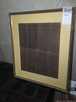 Framed document in dark wood and gold trim, yellow mat board, leaning angled showing full front.