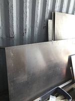 Stacked aluminum sheets leaning against corrugated metal wall