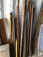 Wide view of various sizes of metal angle irons stacked against a wall, showing rusty and weathered surfaces, some painted yellow.