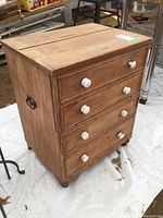 Front-left angled view of the antique wooden cabinet showing four drawers with white knobs and side metal handle.