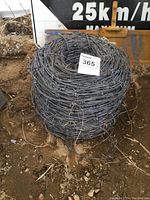 Top view of a tightly coiled roll of galvanized barbed wire with attached lot tag.