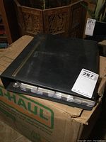 Photo of black 3-ring binder sitting on a U-Haul box, showing lot container