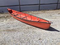 Full side view of entire orange canoe on gravel
