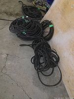 Full view of several coils of black armour covered wiring on concrete floor and leaning against plywood wall.