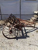Wide view of antique farm implement showing full length frame, two large spoked wheels, and soil cultivation tines beneath.