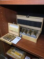 Wide view showing two wooden cases each holding sets of Forstner bits arranged neatly inside on a wooden shelf.