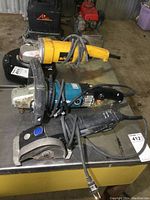 Photo showing three power tools including Dewalt DW840 grinder, Makita grinder, and Dremel Ultra Saw arranged on table.