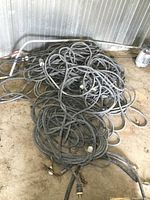 Pile of tangled black heavy gauge cords on concrete floor