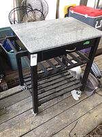 Full view of the kitchen island showing the granite top, wooden frame, wheels and slatted shelves.