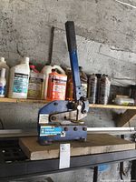 Blue Power Fist metal shear placed on a workbench with various fuel additives and sprays in the background.