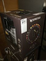 Photo of the closed box showing the full Nespresso Vertuo machine packaging, branding, and model information.