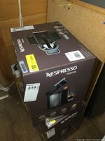 Photo of closed Nespresso Vertuo machine boxed upright against wood wall.