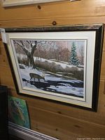 Framed oil painting on board of a winter deer scene hung on wood-paneled wall.