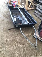 Overall view of resin black sleigh with metal frame and long pull handles on dirt surface
