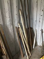 Various square steel tubes, rusted and painted, leaning against a rough masonry wall.