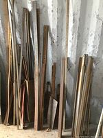 Photo showing a variety of flat steel stock and bars, leaning against a wall, some rusty and weathered.