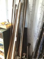 Photo showing various steel pipes leaning against a wall with different diameters and lengths, some rusted and some shinier stainless steel.