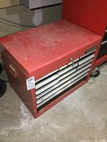 Red Craftsman metal toolbox top box with 12 drawers locked and showing keys, atop concrete floor next to red cart.