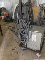 View of Hammond transformer on wheeled metal cart with large coiled cables hanging on side, showing front and side panels with labels.