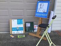 Front view of both easel and chair with visible art paper pads and art supplies on ground and easel.