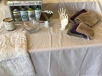Full view of the bathroom accessories and decor items arranged on a beige tablecloth, showing the soap collection box, ceramic hands, towels, candle, and glass bowl with soaps.