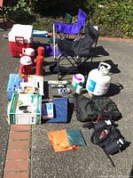 Full view of camping gear lot showing chairs, cooler, thermoses, propane tank, airbed, stove, backpack, fanny pack, poncho, and accessories.