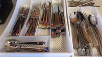 Flatware set including forks, spoons, knives stored in white plastic organizer with additional cutlery pieces