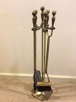 Full set of brass fireplace tools in stand against wall