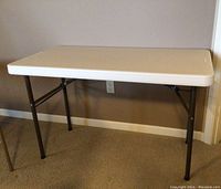 Full view of folding table showing white plastic surface and metal legs.