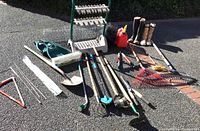 Overview of the garden tools laid out on driveway including boots, gas can, and various long-handled tools
