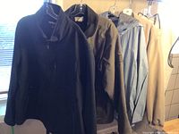 Four men's jackets hanging on a rack in natural light, showing colors, styles, and general condition.