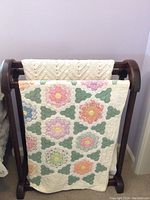 Wooden quilt rack with two throws: the floral quilt in front and the crocheted throw behind it on top bar.