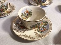 Close-up of teacup and saucer set showing intricate painted classical figures and 22k gold accents.