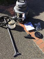 Shop-Vac wet/dry vacuum with main canister, hose, extension wand, floor nozzle, filter, and manuals spread out on ground.