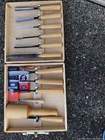Full wood carving chisel set including six chisels with wooden handles, wooden mallet, sharpening stone, sharpening compound, and oil stored in a light wooden carrying case.