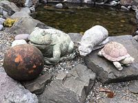 View of all four items by pond: terracotta sphere, frog statue, raccoon statue, turtle statue.