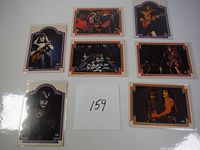 Seven vintage KISS trading cards laid out on white background showing different images of band members Gene Simmons, Paul Stanley, Peter Criss, and Ace Frehley in costume and makeup with musical instruments and stage presence.