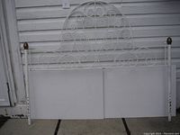 White decorative metal trellis with ornate scrollwork and brass finials on the two upright posts