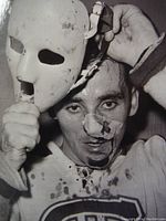 Black and white image of Jacques Plante holding a white goalie mask while wearing a hockey jersey, highlighting the vintage goalie mask.