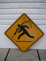 Diamond-shaped warning sign with a black pictogram of a person being hit by a falling tree branch on yellow background.