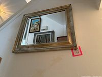 Photo of the beveled mirror hanging on the wall showing reflections of paintings and part of the room.