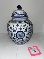 Front view of large blue and white ginger jar with intricate floral and vine designs, capped with matching lid and blue finial.