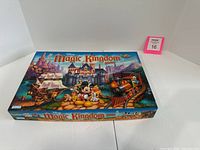 Closed box of Disney Magic Kingdom board game showing colorful Disney characters and theme park images.