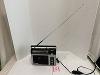 General Electric Superadio II AM/FM radio in black color with extended telescoping antenna. Power adapter plugged in and visible. Radio placed on white background for clear view.