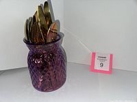 Gold tone flatware in a purple textured glass vase, showcasing forks, knives, and spoons arranged inside.