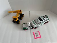 Photo showing the Hess semi-truck with car carrier trailer and white race car, alongside the yellow toy crane on a white background.